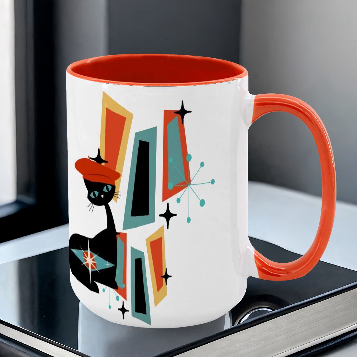 Mid Century Modern coffee mug featuring an atomic cat design with geometric shapes in teal, orange, and black.