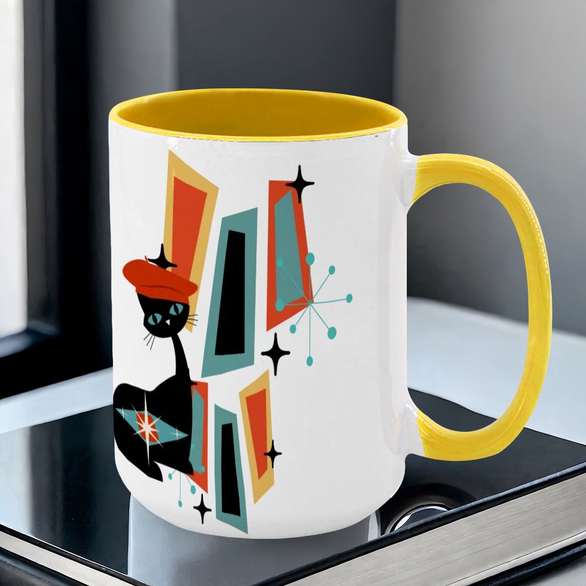 Mid Century Modern coffee mug featuring an atomic cat design with geometric shapes in teal, orange, and black.