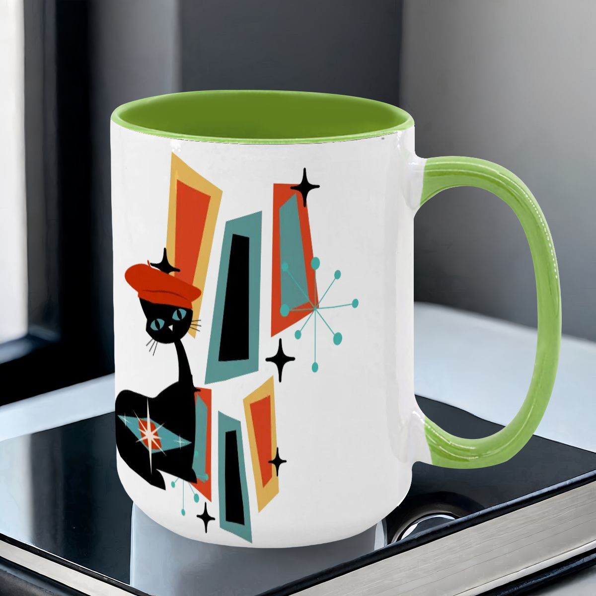 Mid Century Modern coffee mug featuring an atomic cat design with geometric shapes in teal, orange, and black.