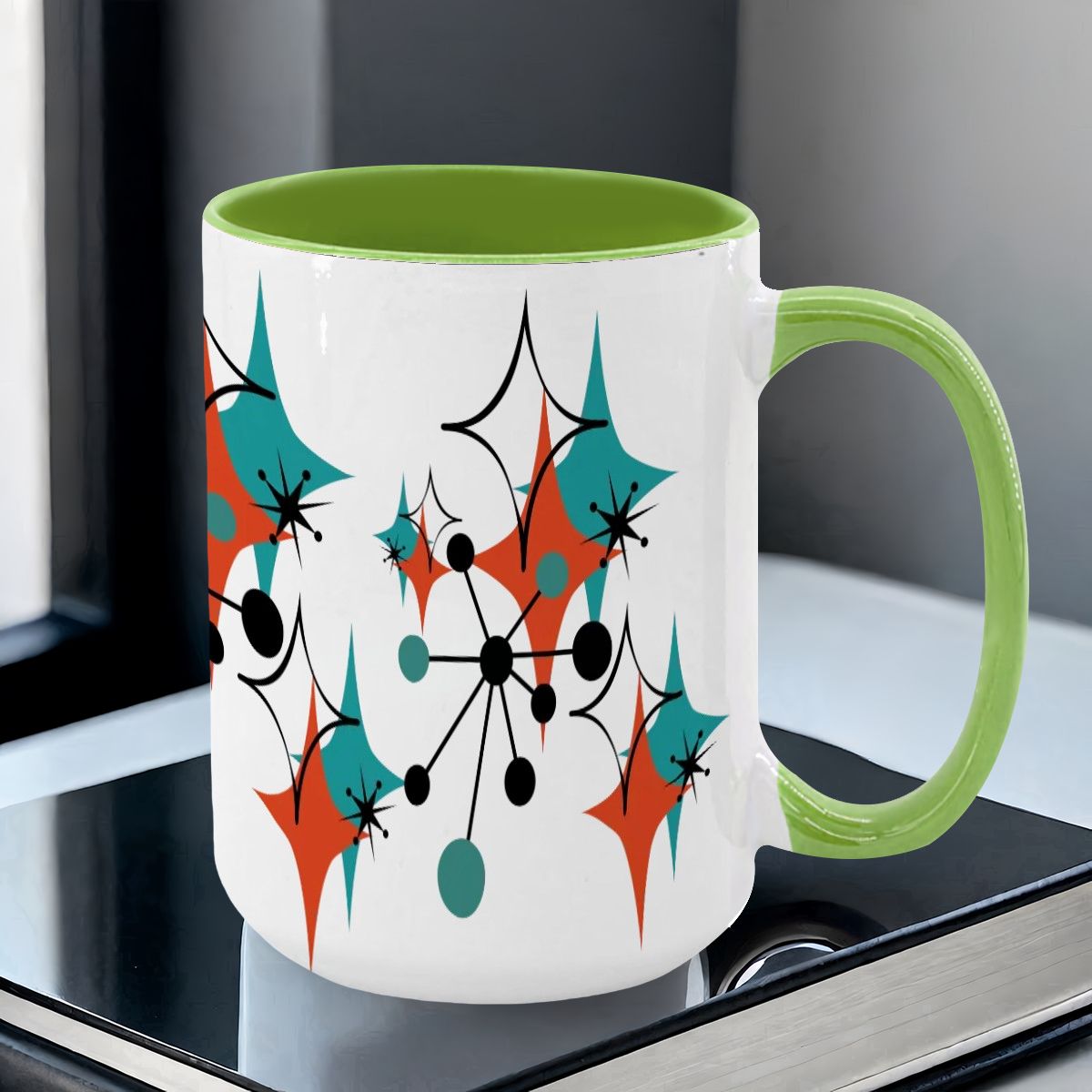 Colorful 15oz mug featuring a Mid Century Modern atomic starburst design in teal, orange, and black with a green handle.